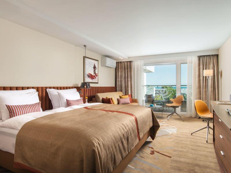 Světý hotelový pokoj s manželskou postelí, posezením a balkonem s výhledem na moře.