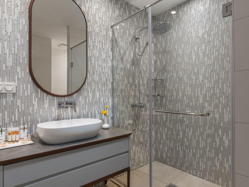 Moderní koupelna se dřezem na skříňce, oválným zrcadlem a sprchovým koutem se skleněnou stěnou.