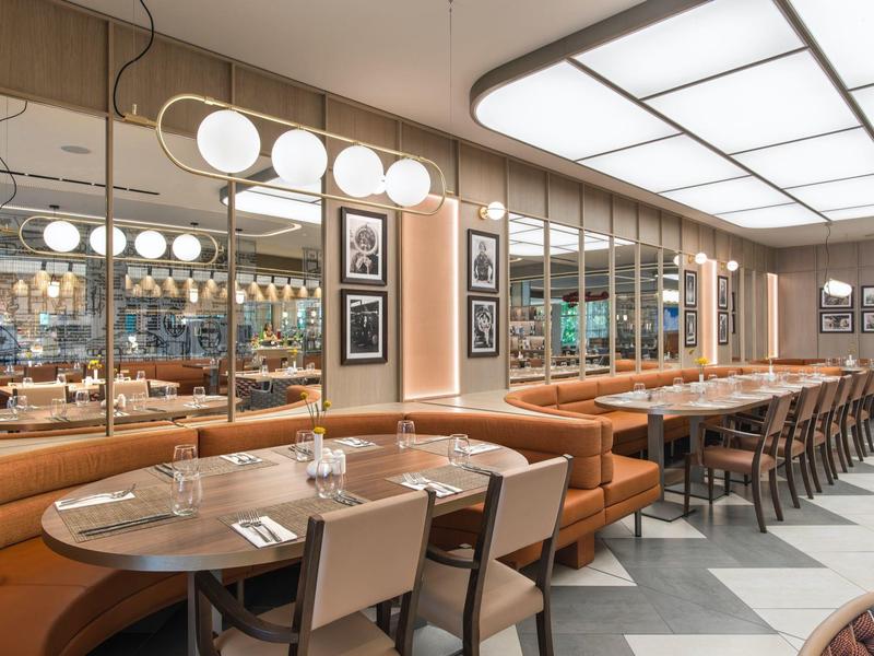 Moderní restaurace s kulatými stoly, koženými sedadly a velkým zrcadlem na stěně.