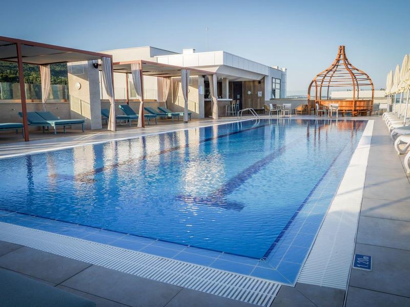 Moderní hotelový bazén s lehátky a otevřenou odpočinkovou zónou za jasné oblohy.