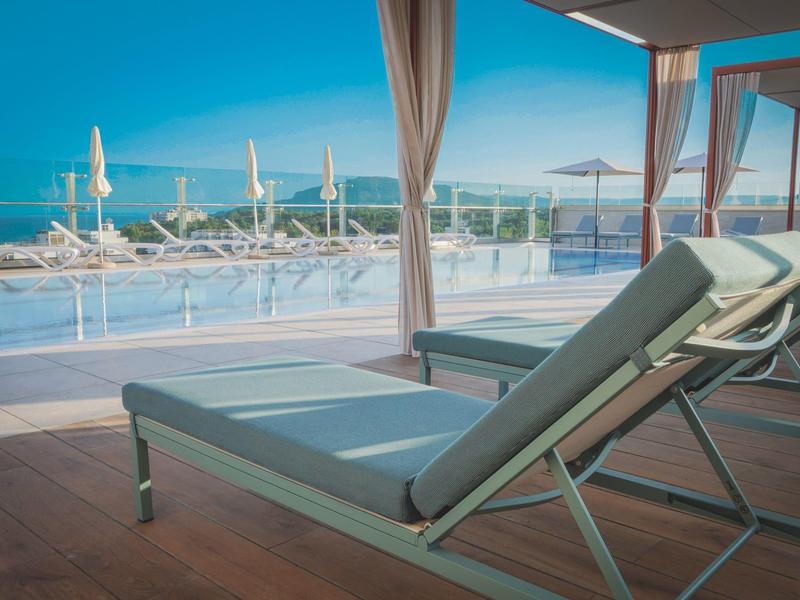 Lehátka na terase s výhledem na bazén a moře za slunečného dne.