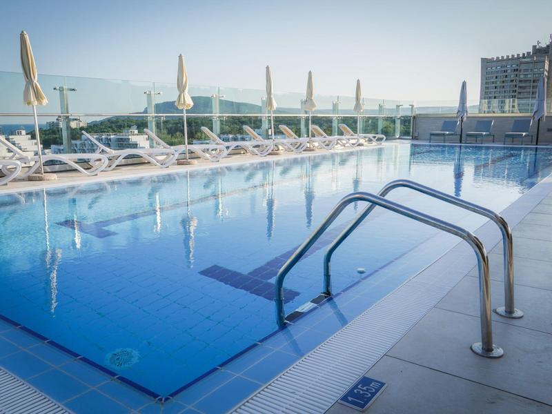 Moderní venkovní bazén na střeše s lehátky a výhledem na město.