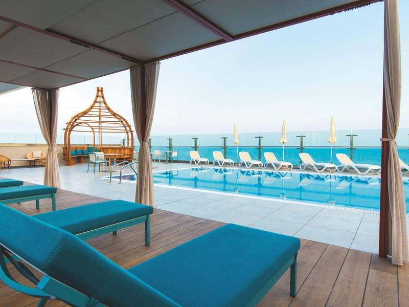 Moderní lehátka a baldachýn s výhledem na bazén a moře v hotelu.