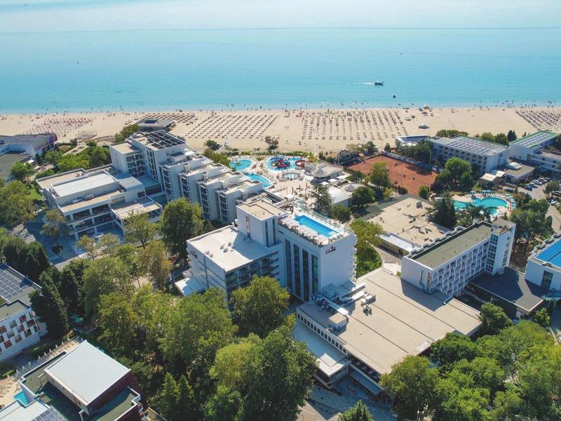 Letecký pohled na plážové letovisko s hotely, stromy a písčitou pláží u moře.