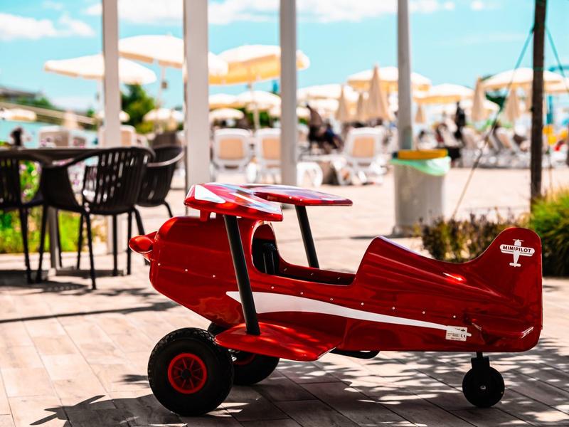 Malé červené dětské letadlo v venkovní části hotelové kavárny za slunečného dne.