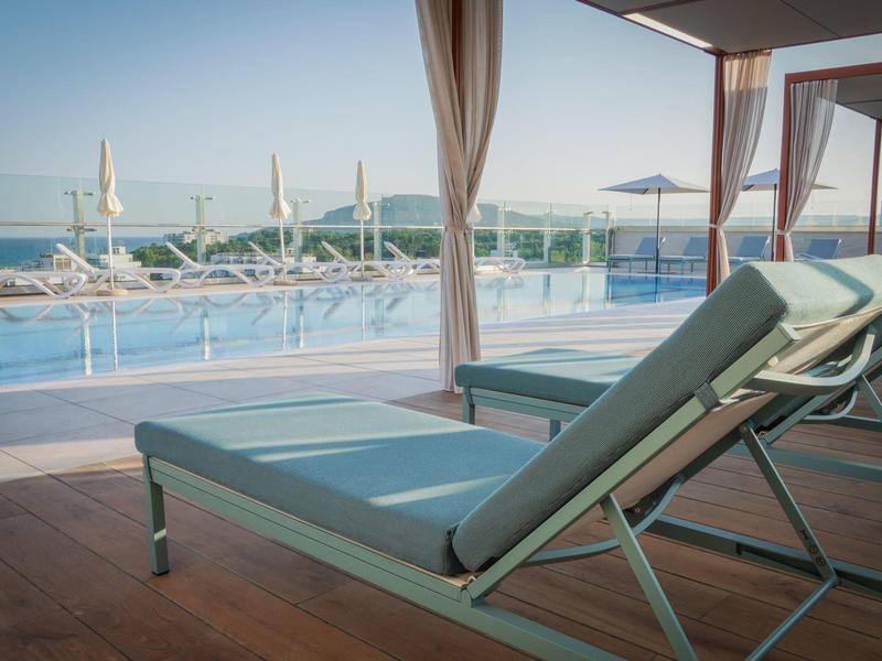 Lehátka u hotelového bazénu s výhledem na moře pod jasnou oblohou.