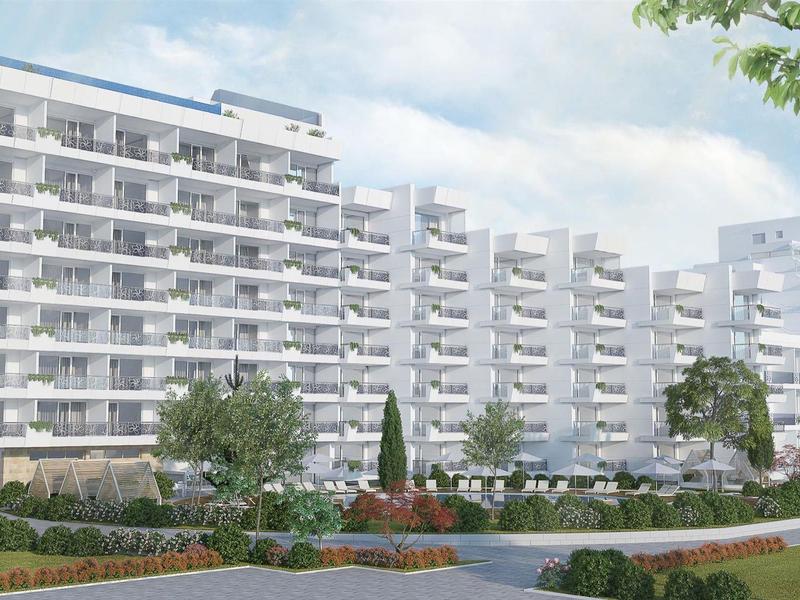 Moderní bytový komplex s velkými balkony a upravenou zahradou za denního světla.