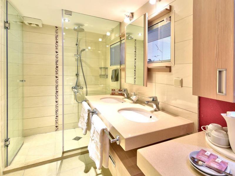 Moderní koupelna se skleněným sprchovým koutem, velkým zrcadlem a bílým umyvadlem za teplého osvětlení.