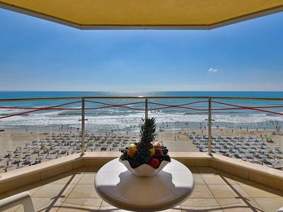 Výhled z balkonu s stolem na pláž s lehátky a moře.