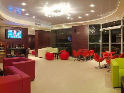 Moderní hotelová lobby s barevnými křesly a odpočinkovými zónami pod jasným stropním osvětlením.