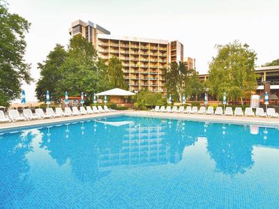 Großer Außenpool mit Liegestühlen, umgeben von Bäumen und mehrstöckigem Hotelgebäude im Hintergrund.