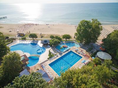 Pohled na plážový hotel s bazénem, lehátky a písečnou pláží u moře.