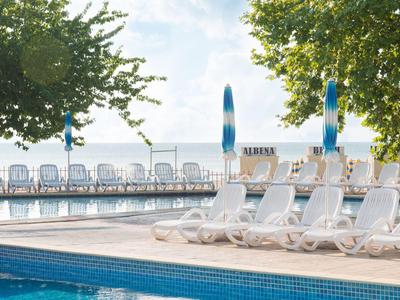 Puste leżaki przy basenie z drzewami w tle w słoneczny dzień.