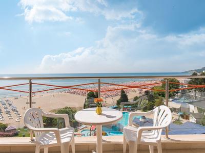 Výhled na moře z balkonu s malým kulatým bílým stolkem a dvěma plastovými židlemi.