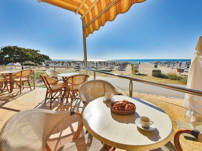 Słoneczny taras hotelowy z stołami, krzesłami i widokiem na plażę i morze.