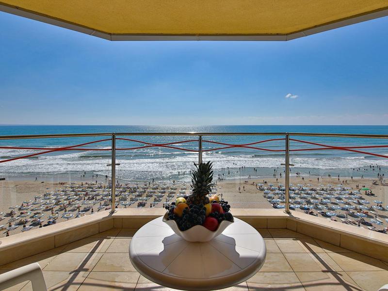 Výhled z balkonu s stolem na pláž s lehátky a moře.