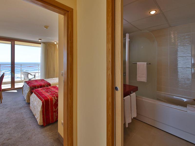 Pohled na hotelový pokoj s výhledem na moře a přilehlou koupelnou s vanou.