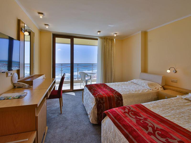 Dvoulůžkový pokoj s výhledem na moře, dvě postele, TV, psací stůl a balkon v hotelu.