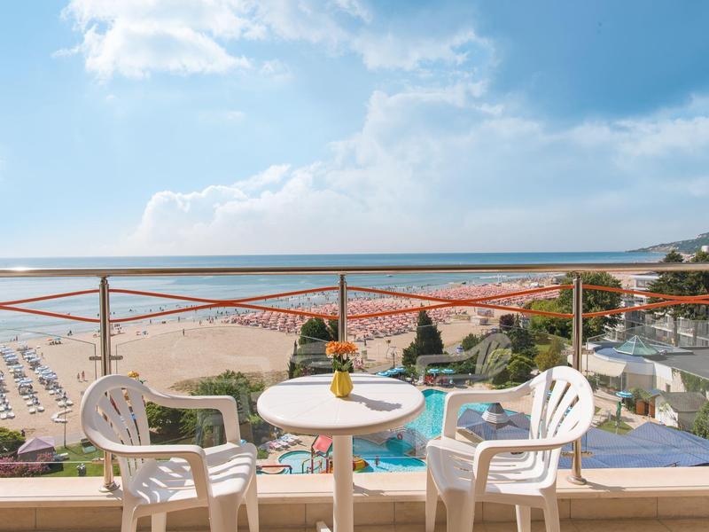 Výhled na moře z balkonu s malým kulatým bílým stolkem a dvěma plastovými židlemi.