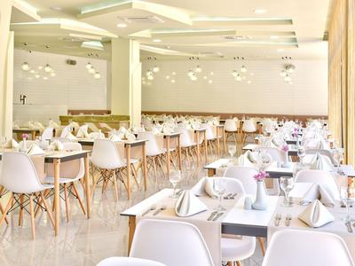 Světla, moderní restaurace s bílými židlemi a prostřenými stoly v prostorném interiéru.