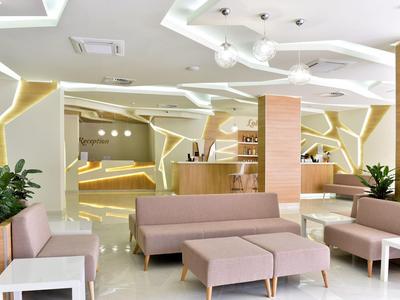 Moderne Lobby mit beigen Sitzmöbeln, hellen Wänden, integriertem Lichtdesign und grünen Pflanzen.