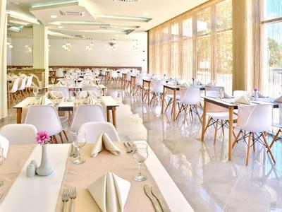 Světlá, moderní jídelna s bílými židlemi a velkými okny vpouštějícími denní světlo.