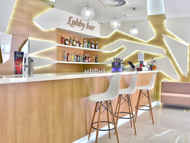 Moderne Bar mit hellem Holz, weißen Stühlen und leuchtenden Wandelementen in warmem Licht.