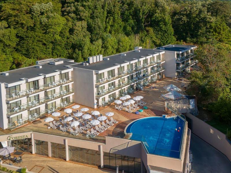 Moderner Hotelkomplex mit Pool und Sonnenschirmen, umgeben von dichter grüner Natur.