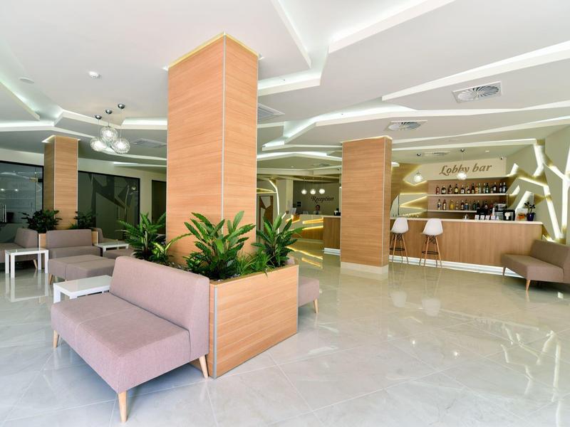 Heller Hotellobby mit weißen Fliesen, rosa Sofas, braunen Säulen und moderner Theke im Hintergrund.