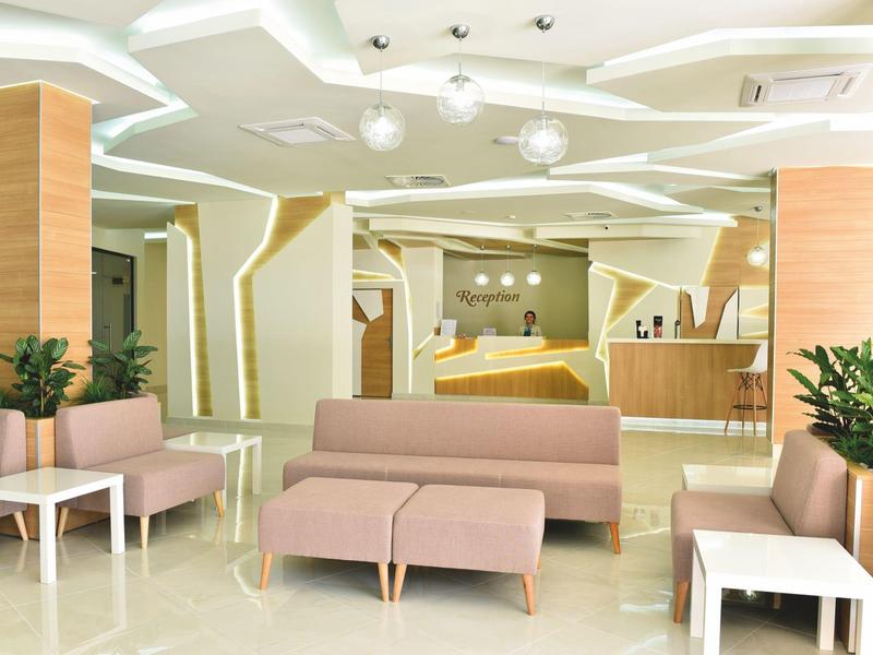 Modern eingerichteter, heller Aufenthaltsraum mit beigen Sofas, weißen Tischen und grünen Pflanzen.