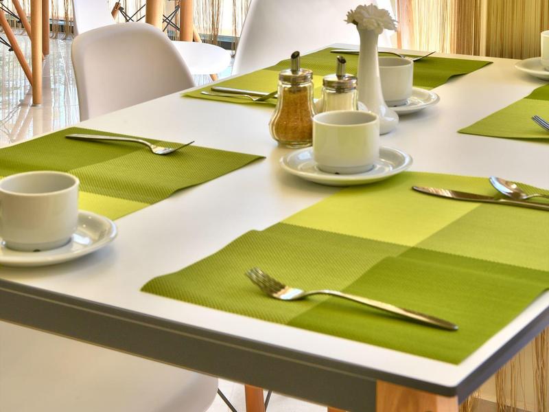 Moderner Essbereich mit weißem Tisch, grünen Platzsets und weißen Stühlen, innen hell und freundlich.