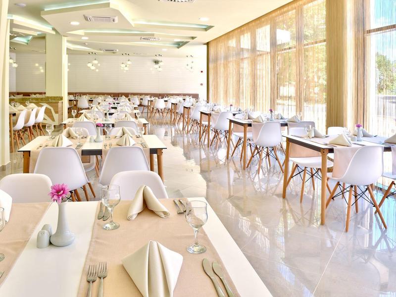 Heller, moderner Speisesaal mit weißen Stühlen, gedeckten Tischen und großen Glasfenstern.