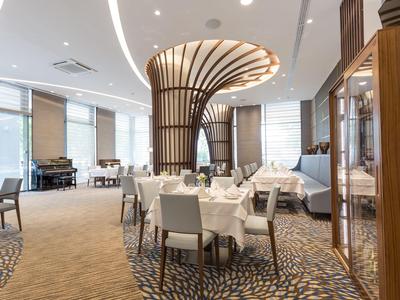 Elegant hotelrestaurant met witte tafels, grijze stoelen en een decoratieve houten pilaar in het midden.