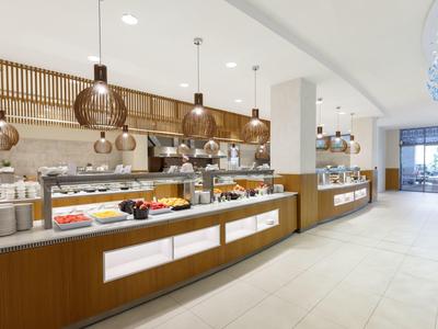 Světlý bufet s rozmanitým jídlem a moderními lampami v prostorné jídelně.