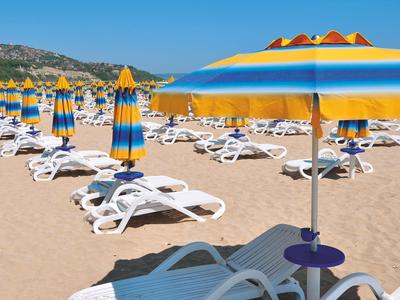 Strand met geel-blauwe parasols en witte ligstoelen op zand bij helder weer.