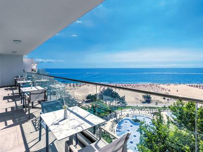 Balkon mit Tischen und Stühlen, Blick auf Sandstrand, Meer und blauen Himmel am sonnigen Tag.