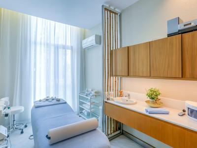 Světelná ošetřovací místnost s lůžkem, skříní a velkým oknem s bílými závěsy.