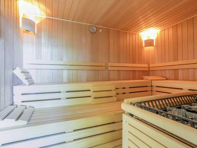 Světelná sauna s dřevěným obložením, lavicemi a kamny na saunu v popředí.