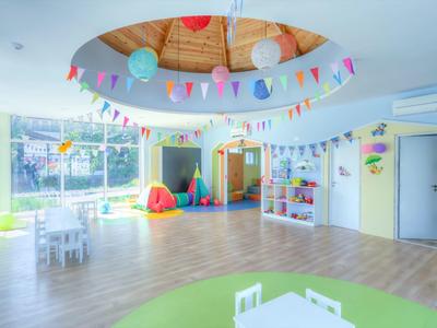 Světlá a barevná dětská herna se stoly, polštáři a velkými okny