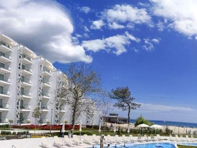 Moderní hotelový komplex s bazénem, palmami a výhledem na útesy pod modrou oblohou.