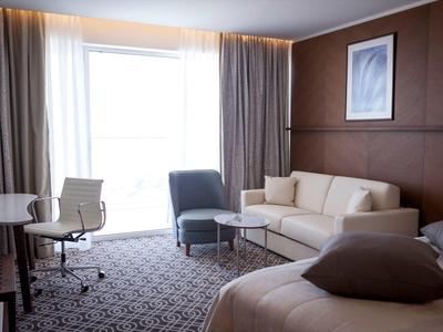 Moderně zařízený hotelový pokoj s postelí, pohovkou, židlemi a velkým oknem.