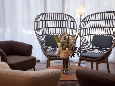 Gezellige zithoek met moderne stoelen, bank en een vaas bloemen voor witte gordijnen.