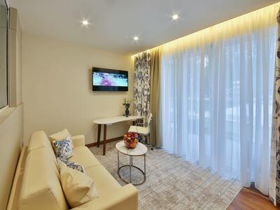 Moderní obývací pokoj s pohovkou, závěsy a TV, světlé osvětlení.