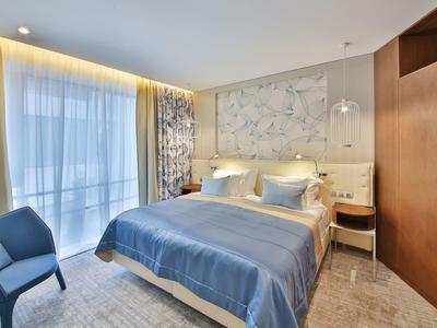 Moderně zařízený hotelový pokoj s velkou postelí, modrou přikrývkou a balkonovým oknem.