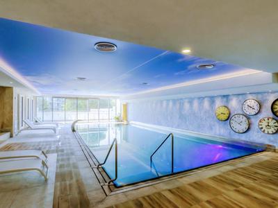 Moderní krytý bazén s lehátky a různými hodinami na zdi.