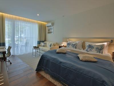 Moderně zařízený hotelový pokoj s velkou postelí, psacím stolem a balkonem se závěsy.