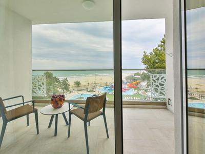 Balkon s stolem a židlemi s výhledem na pláž a moře za zatažené oblohy