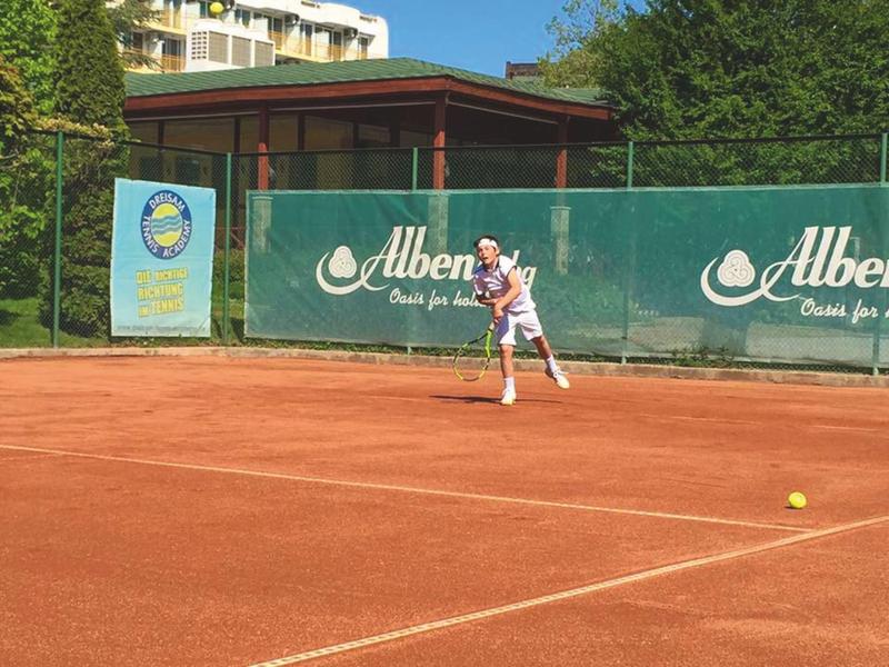Žena hraje tenis na antukovém dvorci za slunečného počasí.