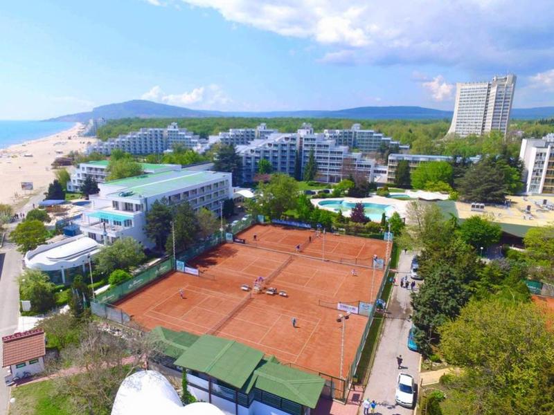 Balkon s stoly a židlemi s výhledem na pláž a moře pod modrou oblohou.