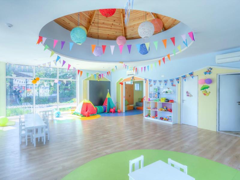 Světlá a barevná dětská herna se stoly, polštáři a velkými okny